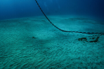 Underwater photo of heavy steel anchor chain that hangs down from water surface and lays on white...