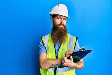 Redhead man with long beard wearing safety helmet holding clipboard skeptic and nervous, frowning upset because of problem. negative person.