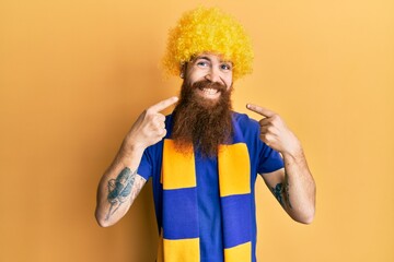 Redhead man with long beard football hooligan cheering game wearing funny wig smiling cheerful showing and pointing with fingers teeth and mouth. dental health concept.