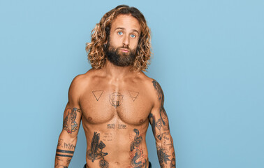 Handsome man with beard and long hair standing shirtless showing tattoos looking at the camera...