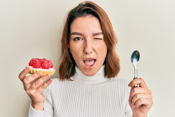 Young caucasian woman holding sweet pastry winking looking at the camera with sexy expression,...