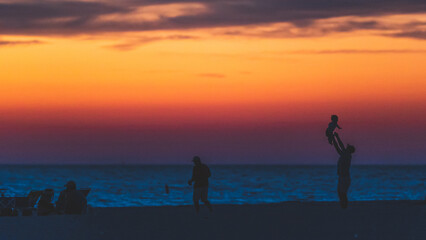 Father throwing child in air at beach, silhouette sunset