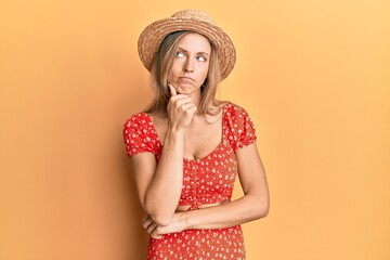 Beautiful caucasian woman wearing summer hat thinking concentrated about doubt with finger on chin and looking up wondering