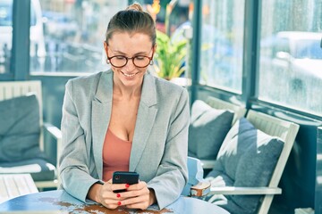 Young blonde businesswoman smiling happy using smartphone at the coffee shop.