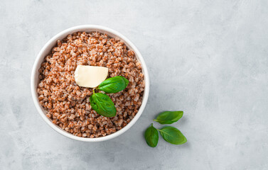 White plate with buckwheat porridge with butter and basil on a gray background.