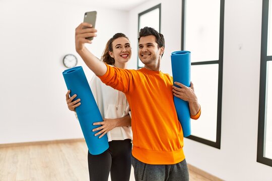 Young hispanic sporty couple holding yoga mat and making selfie by the smartphone at sport center.
