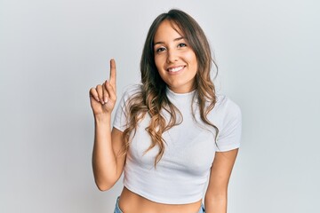 Young brunette woman wearing casual white t shirt showing and pointing up with finger number one while smiling confident and happy.