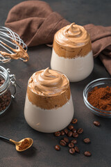 Korean dalgona coffee in two clear glasses on a brown background.