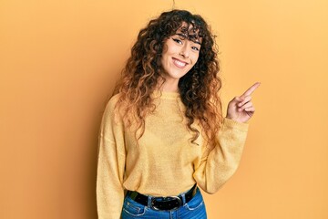 Young hispanic girl wearing casual clothes with a big smile on face, pointing with hand and finger to the side looking at the camera.