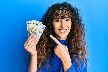 Young hispanic girl holding euro banknotes smiling happy pointing with hand and finger - obrazy, fototapety, plakaty