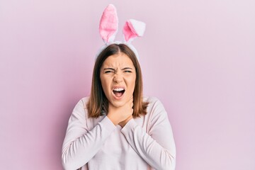 Young beautiful woman wearing cute easter bunny ears shouting and suffocate because painful strangle. health problem. asphyxiate and suicide concept.