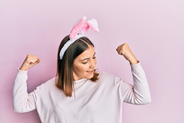 Young beautiful woman wearing cute easter bunny ears showing arms muscles smiling proud. fitness concept.