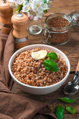 Buckwheat with butter and basil in a white plate on a brown background.