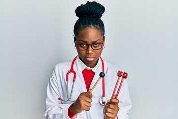 Young african american woman wearing doctor uniform holding tuning fork depressed and worry for...