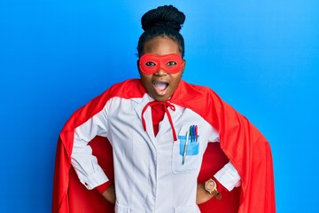 Young african american woman wearing doctor uniform and super hero costume celebrating crazy and...