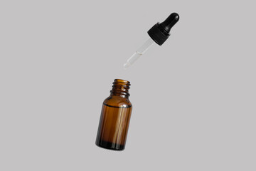 Flying opened brown dropper glass bottle with pipette isolated on gray background. Serum, acid,...