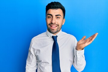 Young hispanic man wearing business clothes smiling cheerful presenting and pointing with palm of hand looking at the camera.