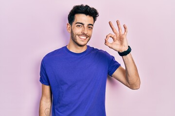 Fototapeta premium Young hispanic man wearing casual t shirt smiling positive doing ok sign with hand and fingers. successful expression.
