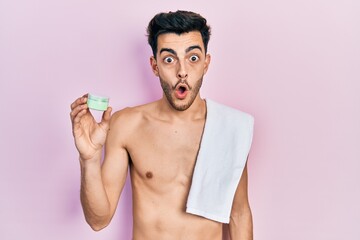 Fototapeta premium Young hispanic man shirtless wearing towel and eye bags patches scared and amazed with open mouth for surprise, disbelief face