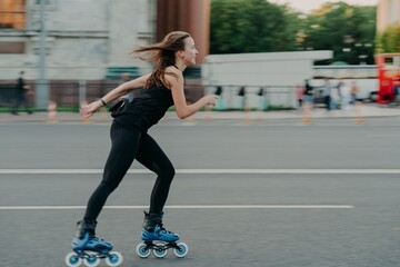 Active leisure concept. Full length shot of young slim woman rollerblades along asphalt on street...