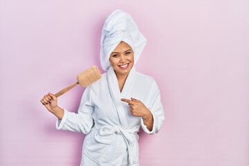 Young hispanic girl wearing bathrobe holding sponge smiling happy pointing with hand and finger