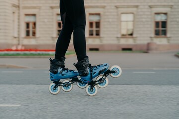 Cropped shot of faceless woman wears rollerblades for riding on road enjoys hobby in fresh air has...