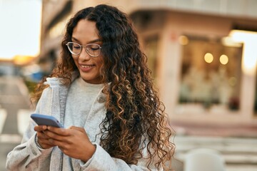Young latin woman smiling happy using smartphone at the city.