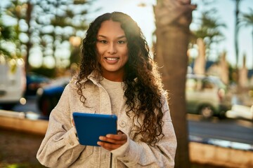 Young latin woman smiling happy using touchpad at the city.