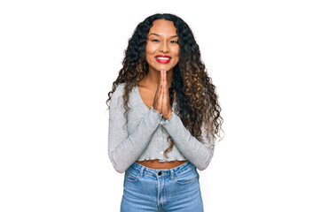 Young hispanic woman with curly hair wearing casual clothes praying with hands together asking for forgiveness smiling confident.