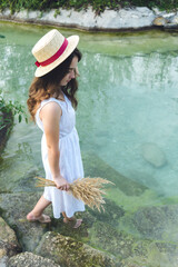 Fototapeta na wymiar A young girl in dress on a sunny day enters the lake. Girl in a straw hat in the river at sunset.
