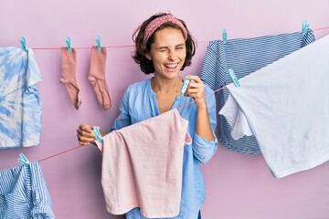 Young brunette woman doing laundry holding tweezers winking looking at the camera with sexy...