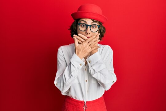 Young brunette woman wearing stewardess style and glasses shocked covering mouth with hands for mistake. secret concept.