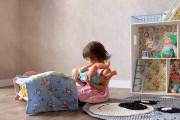 Cute little girl is playing with a doll at home. The child puts the doll to sleep in a toy bed....
