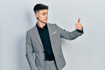 Young caucasian boy with ears dilation wearing business jacket looking proud, smiling doing thumbs up gesture to the side