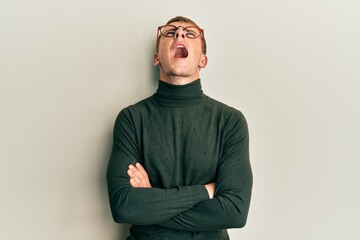 Young caucasian man wearing glasses with arms crossed gesture angry and mad screaming frustrated and furious, shouting with anger looking up.