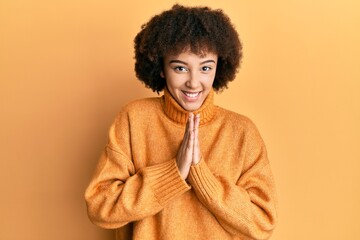 Young hispanic girl wearing wool winter sweater praying with hands together asking for forgiveness smiling confident.