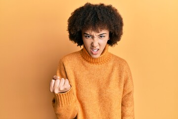 Young hispanic girl wearing wool winter sweater angry and mad raising fist frustrated and furious while shouting with anger. rage and aggressive concept.