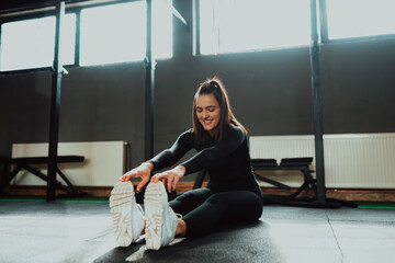 Fit and healthy young woman in sportswear sitting alone on a gym floor stretching on an exercise mat. Selective focus 
