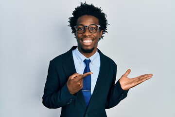 Young african american man wearing business suit amazed and smiling to the camera while presenting with hand and pointing with finger.