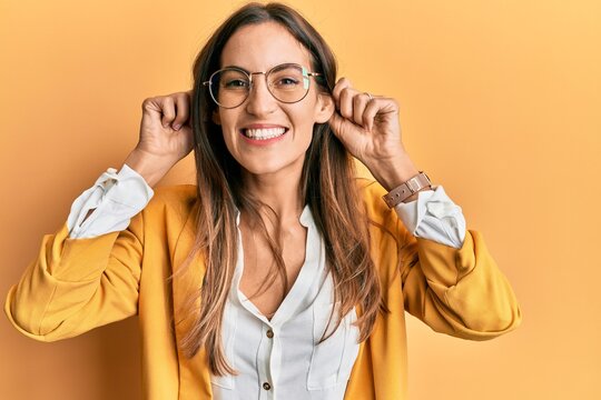 Young beautiful woman wearing business style and glasses smiling pulling ears with fingers, funny gesture. audition problem