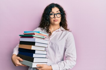 Young brunette woman with curly hair holding a pile of books relaxed with serious expression on face. simple and natural looking at the camera.
