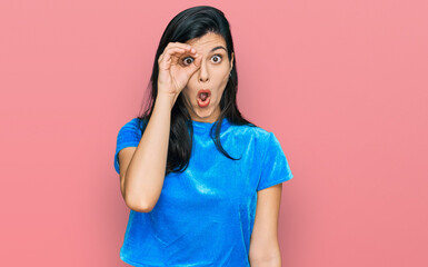 Young hispanic woman wearing casual clothes doing ok gesture shocked with surprised face, eye looking through fingers. unbelieving expression.