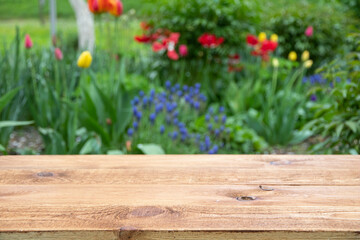 Empty wooden table with free space among flowers in the garden, green blurred background. For product display montage. 