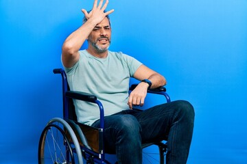 Fototapeta premium Handsome middle age man with grey hair sitting on wheelchair surprised with hand on head for mistake, remember error. forgot, bad memory concept.