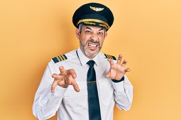 Handsome middle age man with grey hair wearing airplane pilot uniform smiling funny doing claw gesture as cat, aggressive and sexy expression