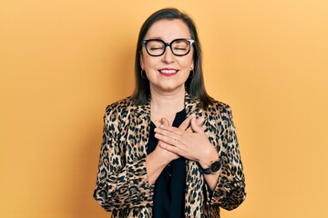 Middle age hispanic woman wearing business clothes and glasses smiling with hands on chest with closed eyes and grateful gesture on face. health concept.