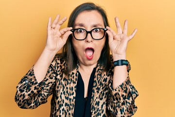 Middle age hispanic woman wearing business clothes and holding glasses afraid and shocked with...