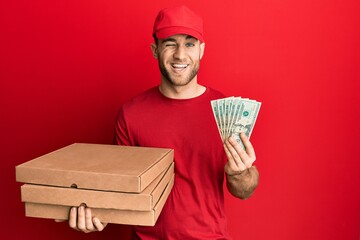 Young caucasian man holding take away food and 20 dollars winking looking at the camera with sexy...