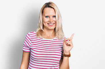 Young caucasian woman wearing casual clothes with a big smile on face, pointing with hand finger to the side looking at the camera.