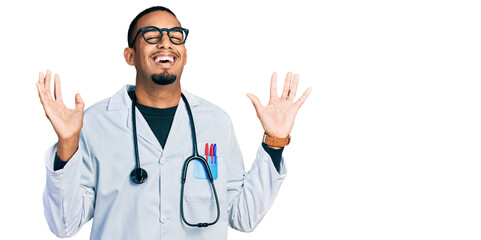 Young african american man wearing doctor uniform and stethoscope celebrating crazy and amazed for success with arms raised and open eyes screaming excited. winner concept